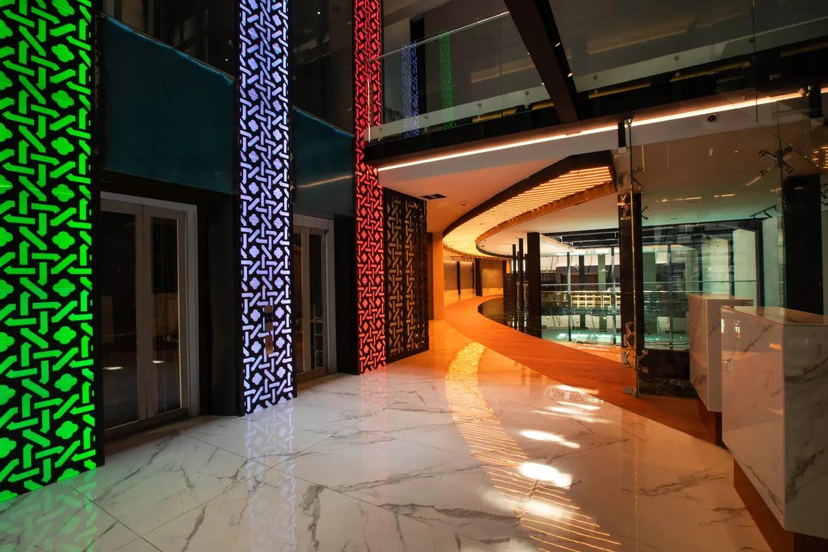 A striking view of the Hotel Catedral lobby, featuring sleek elevators with colorful illuminated panels, polished marble floors, and a contemporary curved ceiling design, creating an atmosphere of modern luxury and sophistication.