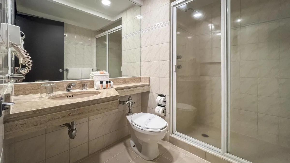 Salle de bain de la chambre standard de l'Hôtel Catedral. Toilettes et lavabo visibles. Au-dessus du lavabo, il y a un miroir et des articles de toilette.