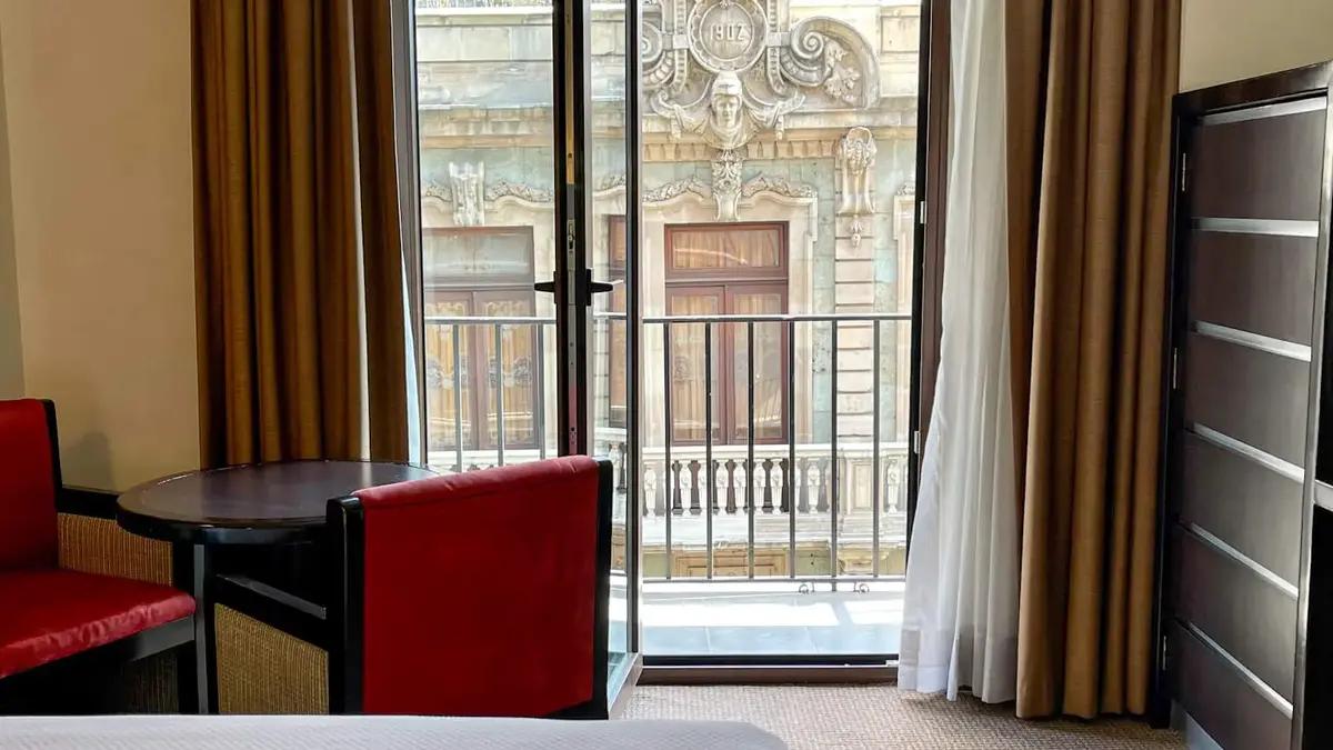 Vista de la habitación del Hotel Catedral. La cama está en el centro y hay una silla visible. Hay una catedral de fondo.