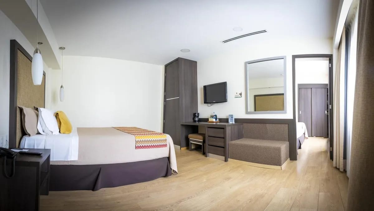 Wide view of the family room from Hotel Catedral. There is an entrance door to the other room with two beds. The colors are warm. Wooden floors.