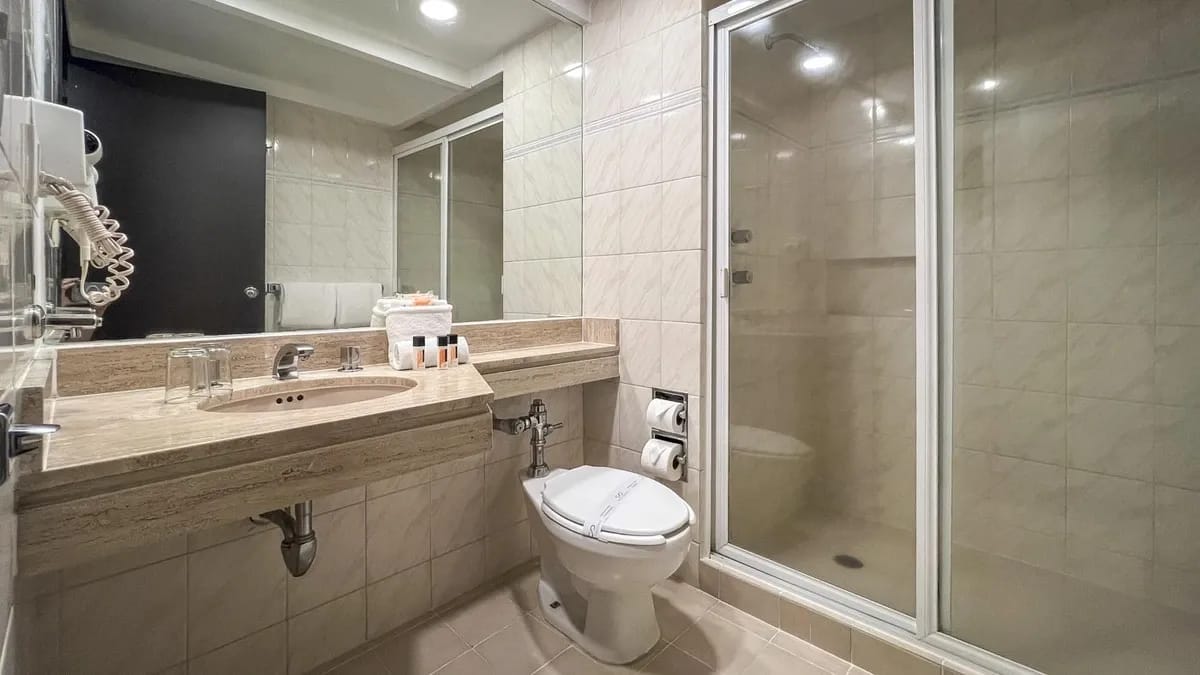 Standard room bathroom from Hotel Catedral. Toilet and sink are visible. Atop the sink there is a mirror and amenities.